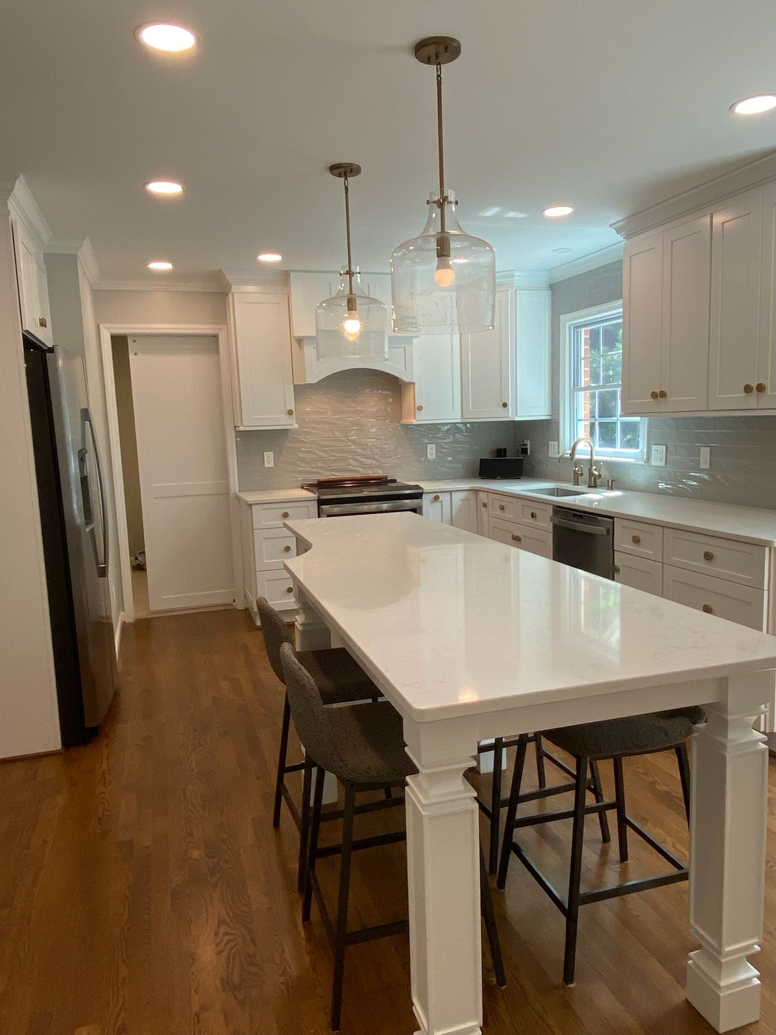 Bright white kitchen with large island, pendant lights, stainless steel appliances, and wood floor.