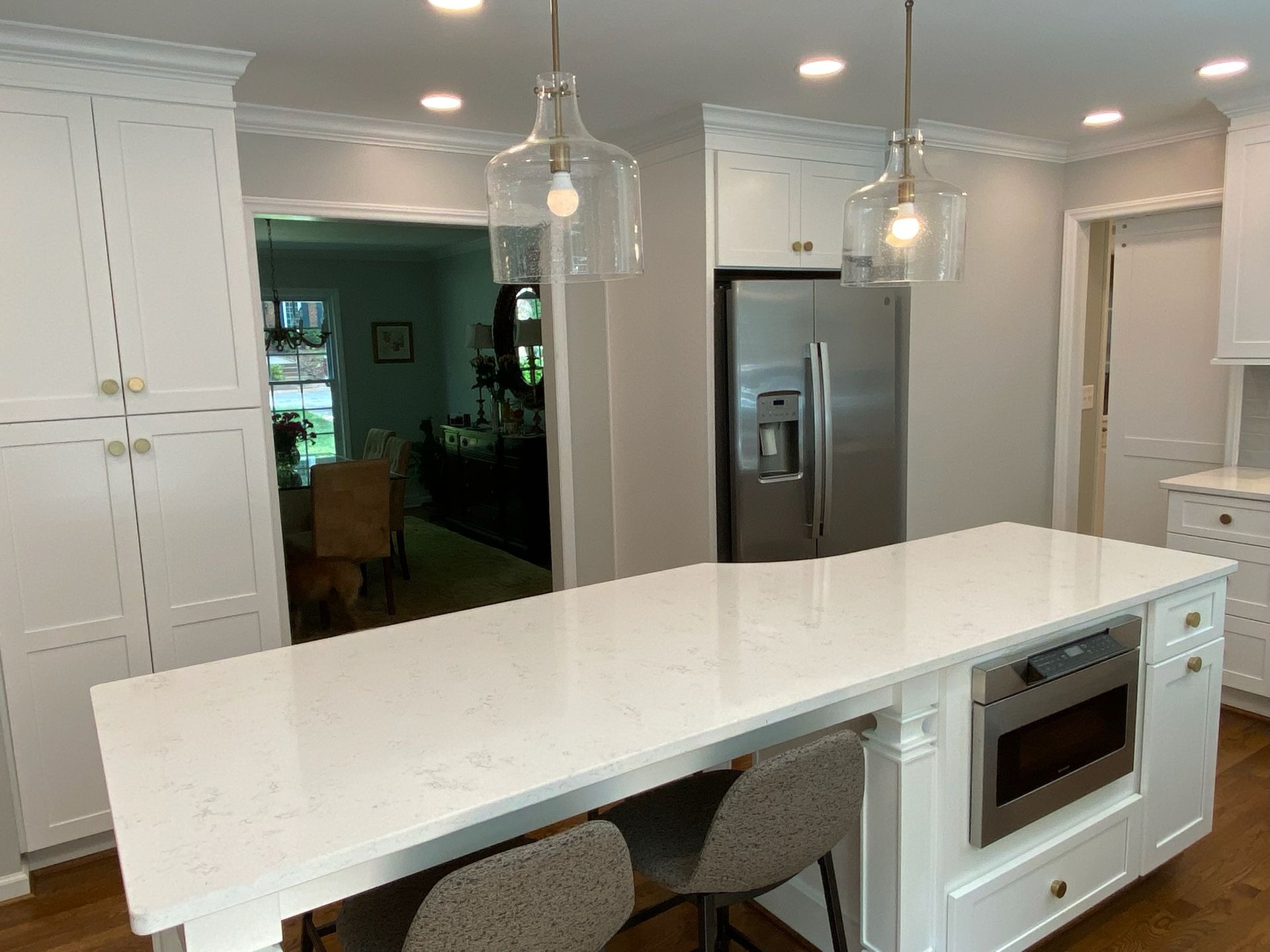 White kitchen with island, quartz countertop, pendant lights, stainless steel appliances, and built-in microwave.