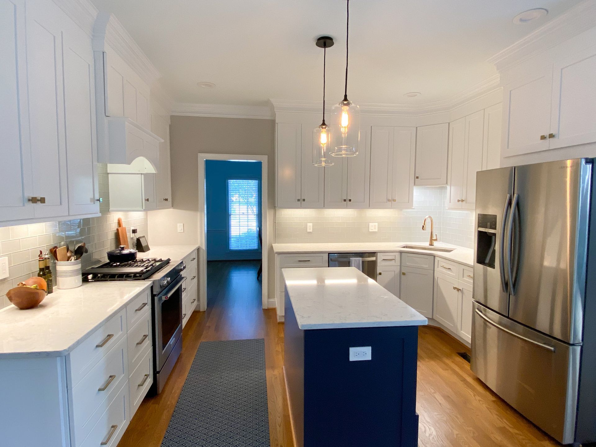White kitchen with blue island, stainless steel appliances, and gold hardware.