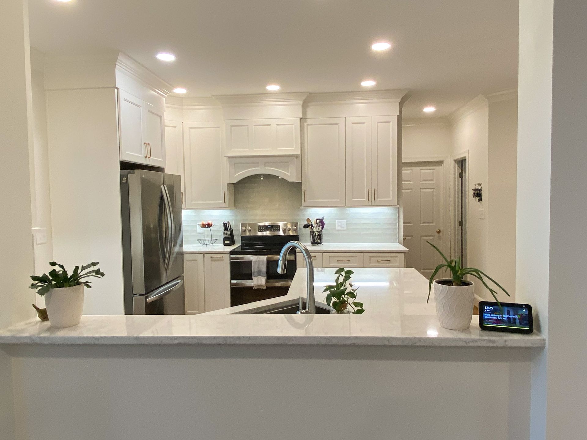 White kitchen with stainless steel appliances, countertop, and overhead lighting.