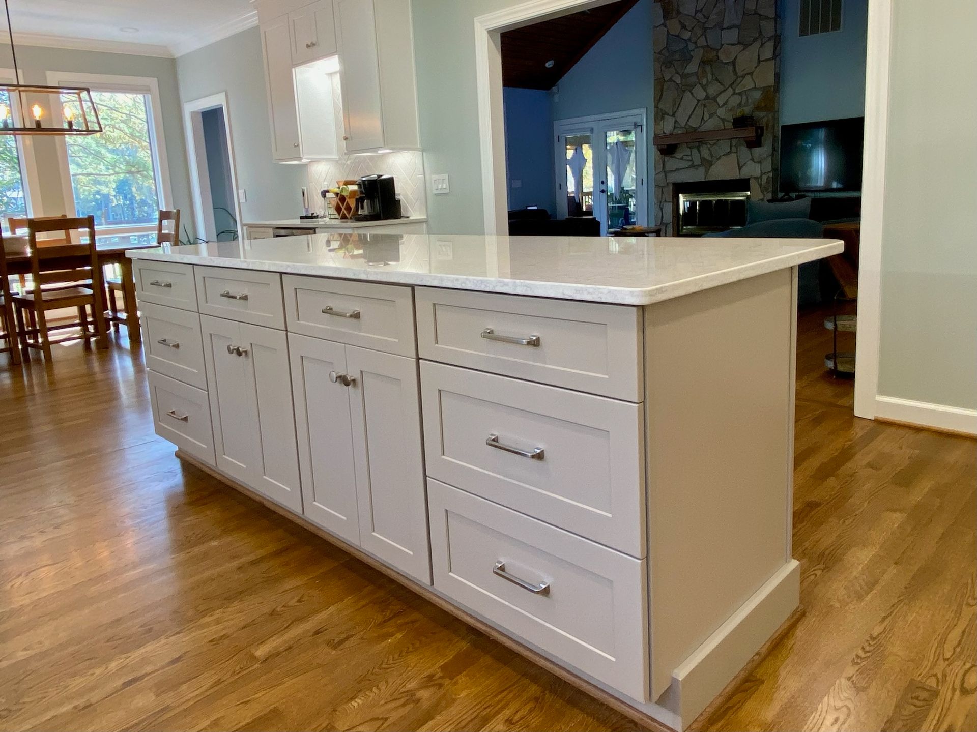 White kitchen island with cabinets and drawers, topped with a white countertop, set on a hardwood floor.