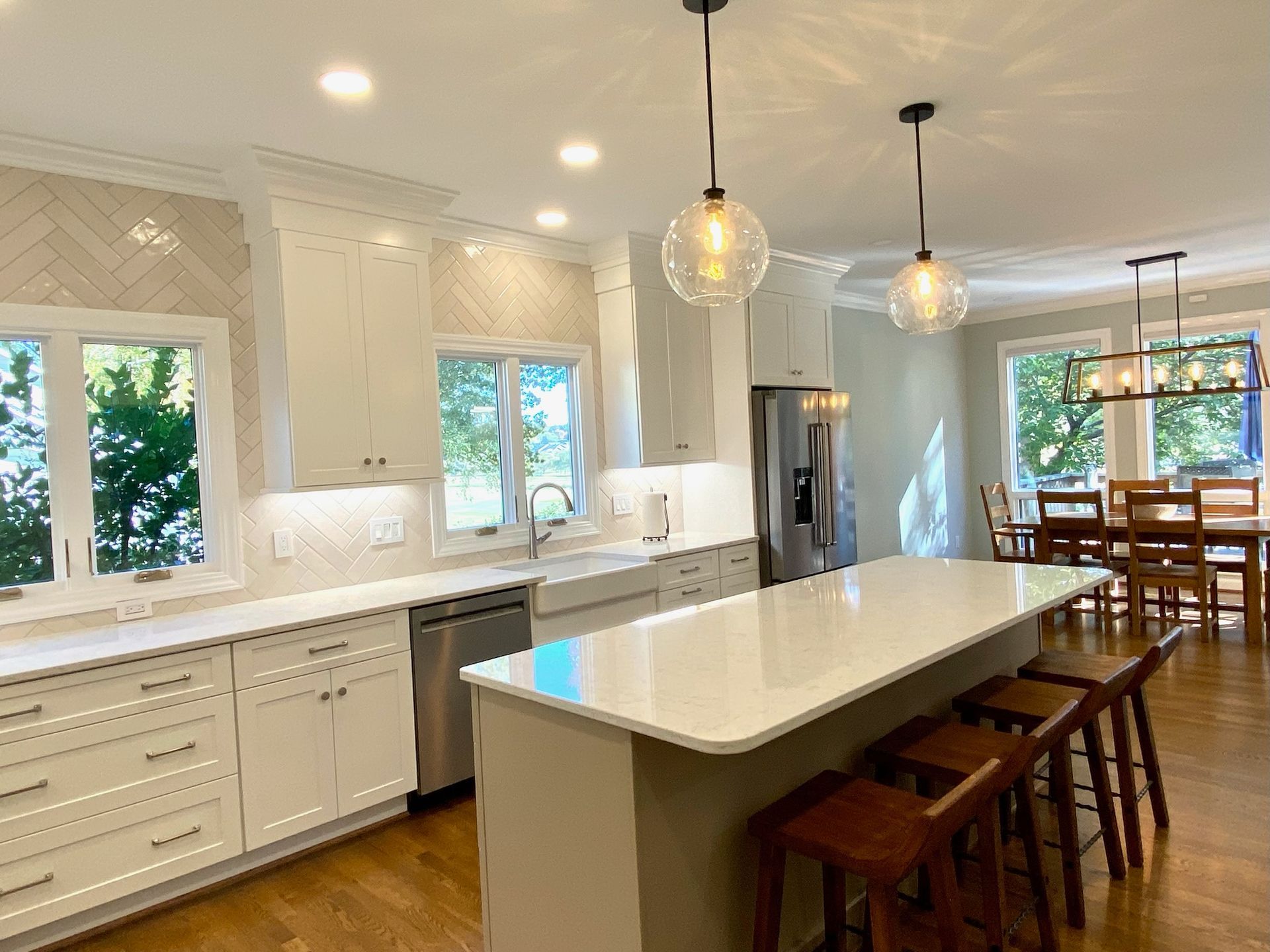 Modern white kitchen with a large island, stainless steel appliances, and wooden flooring.