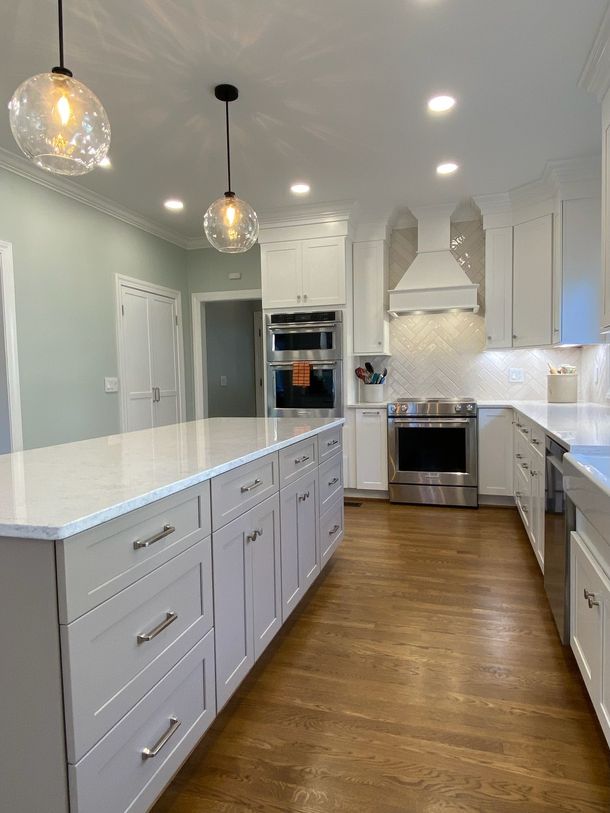 Modern white kitchen with a large island, stainless steel appliances, and wooden floors.