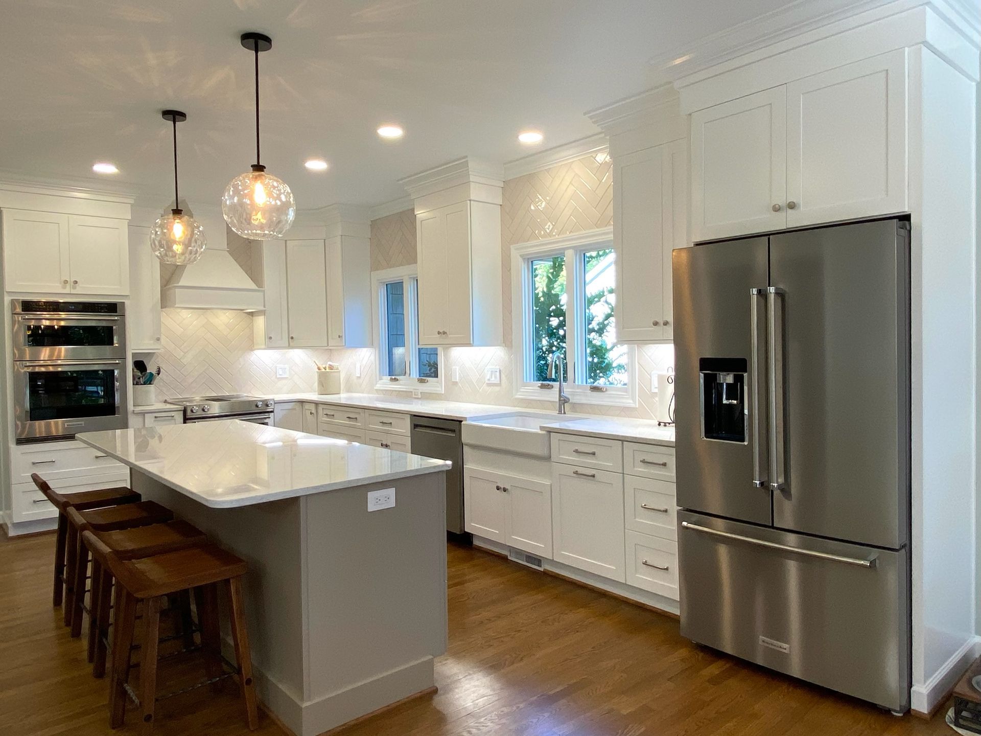 Modern white kitchen with stainless steel appliances, island with stools, and pendant lights.