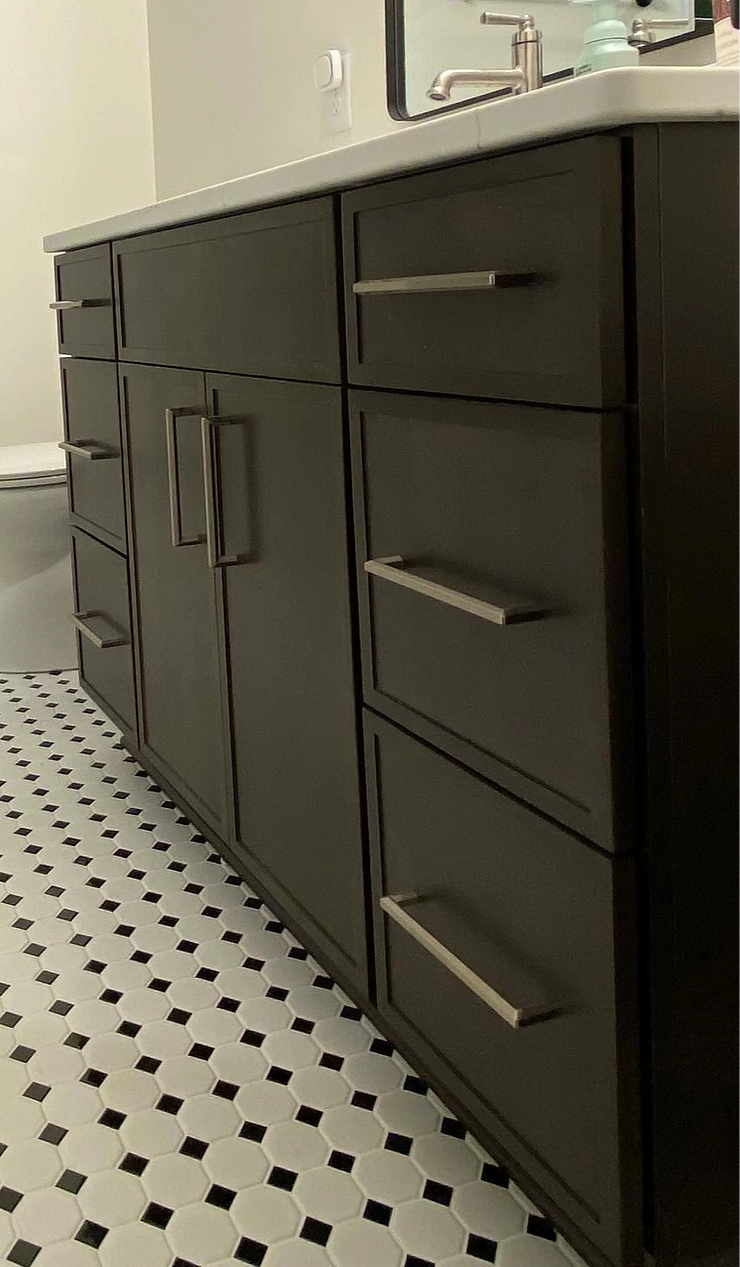 Dark gray bathroom vanity with silver hardware against black and white tiled floor.