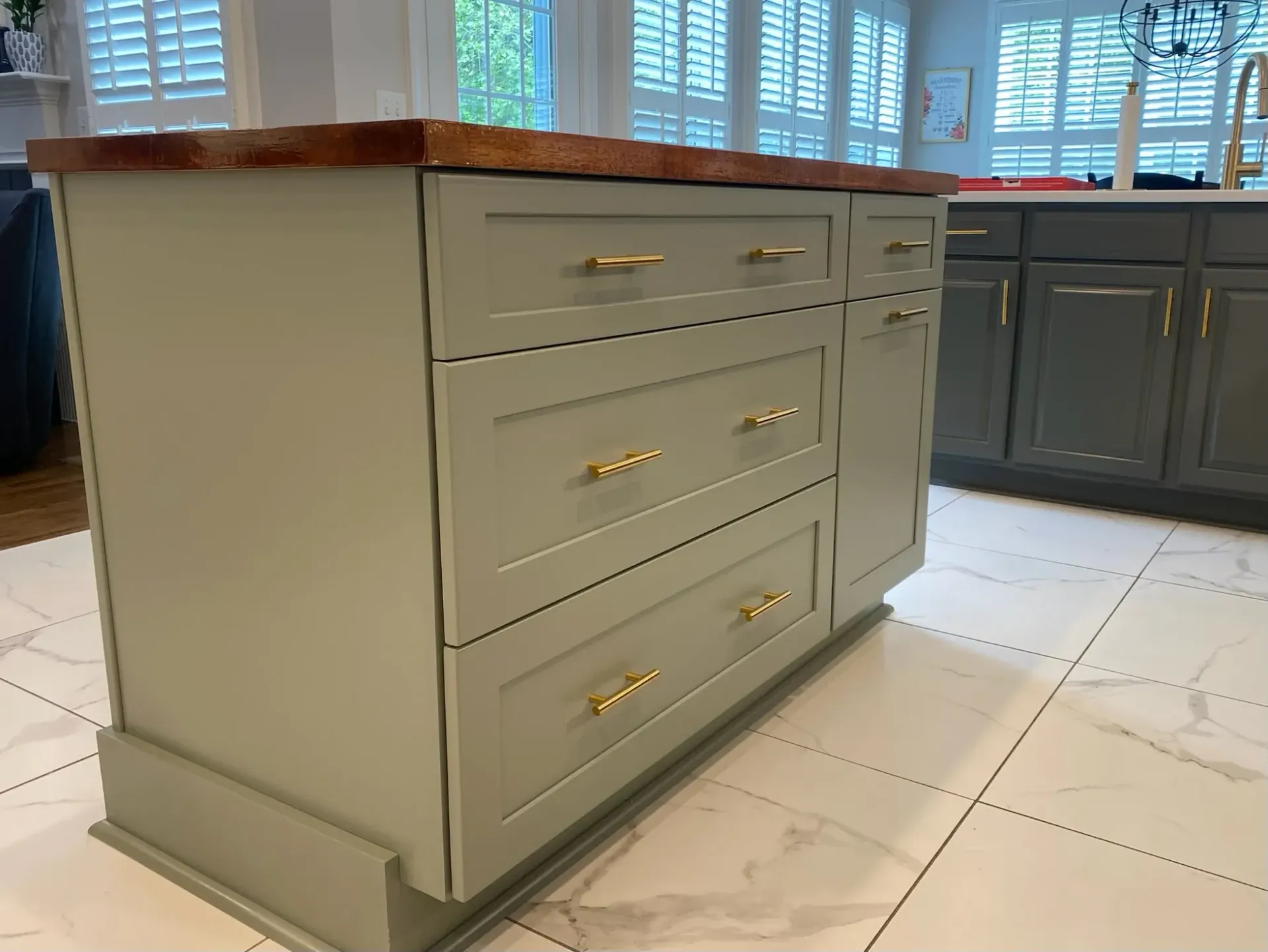Kitchen island with gray cabinets, wood countertop, gold hardware.