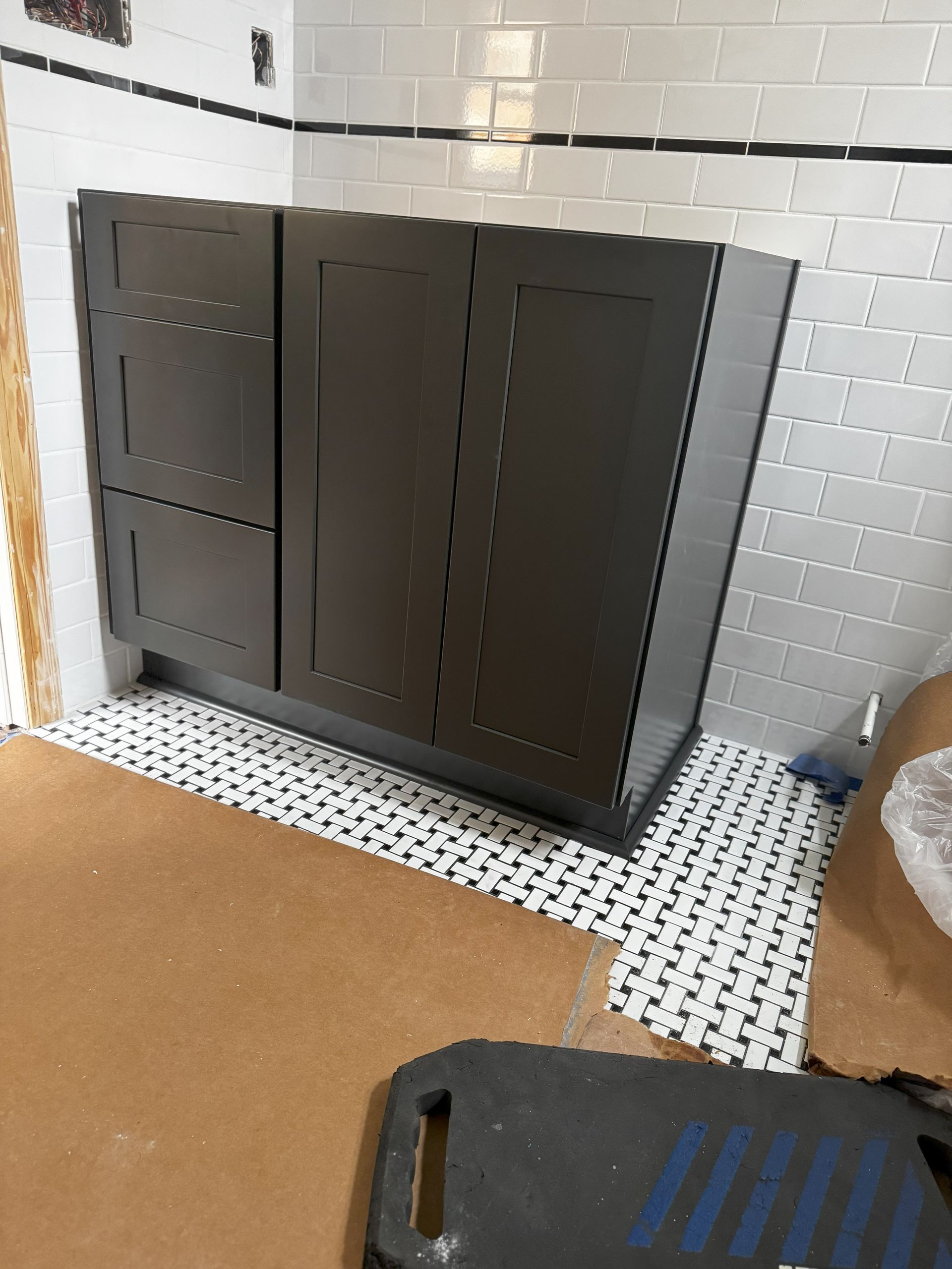Dark brown bathroom vanity cabinet against white tiled wall and black and white floor tiles.