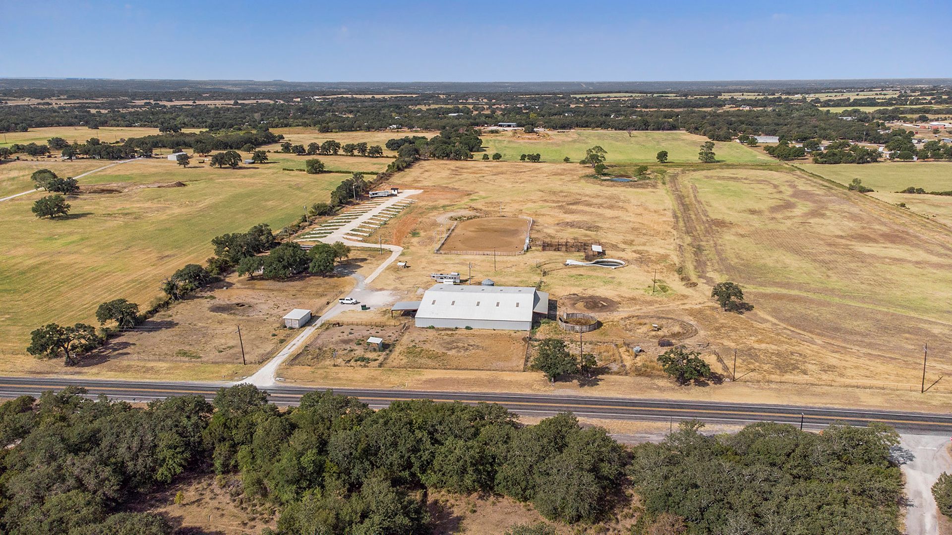 An aerial view of a farm with a house in the middle of a field surrounded by trees.