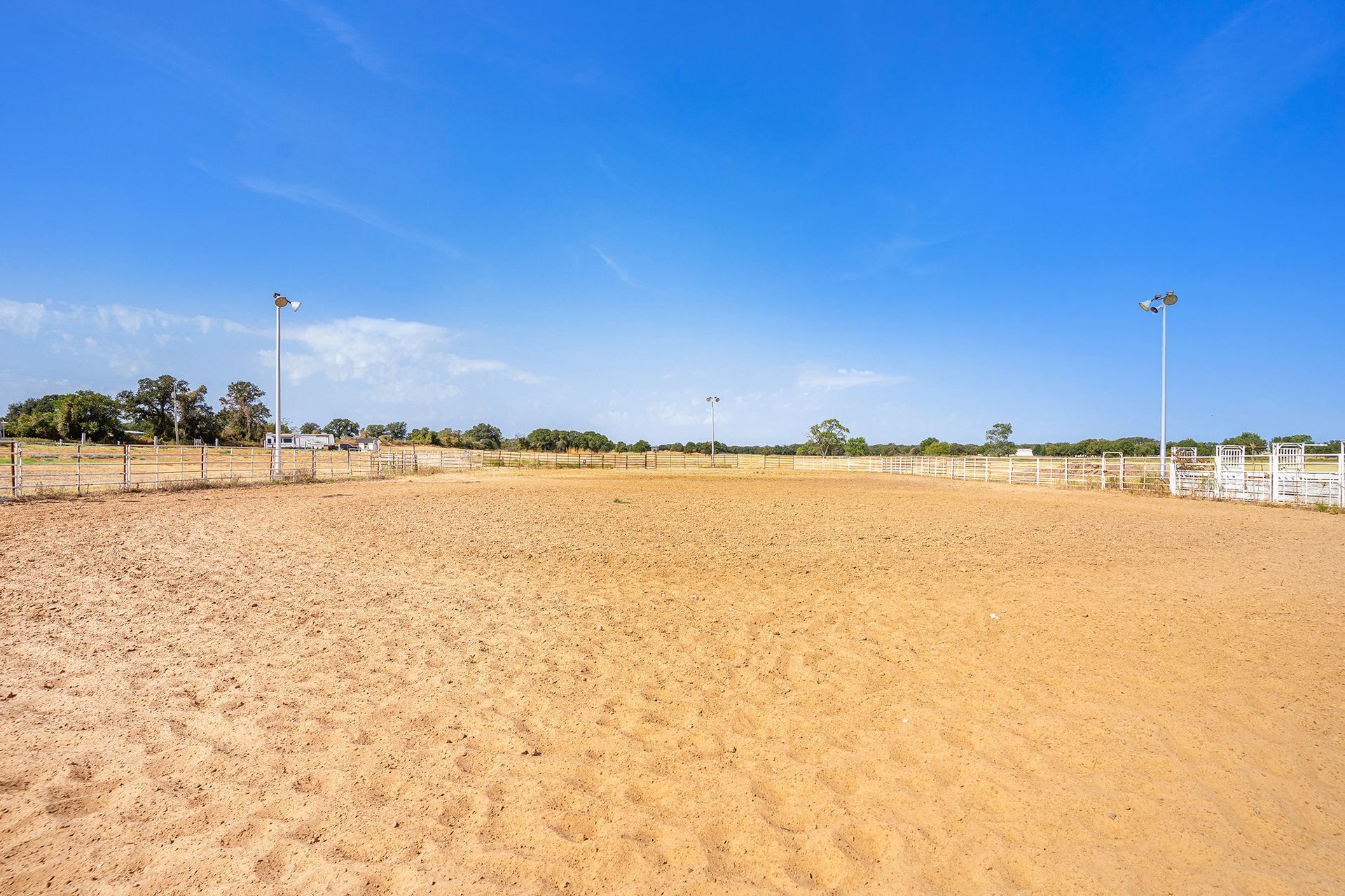 An empty dirt arena with a white fence and a blue sky in the background.