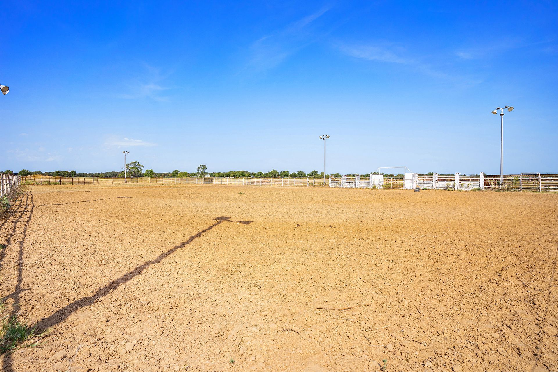 An empty dirt field with a white fence and a blue sky in the background.