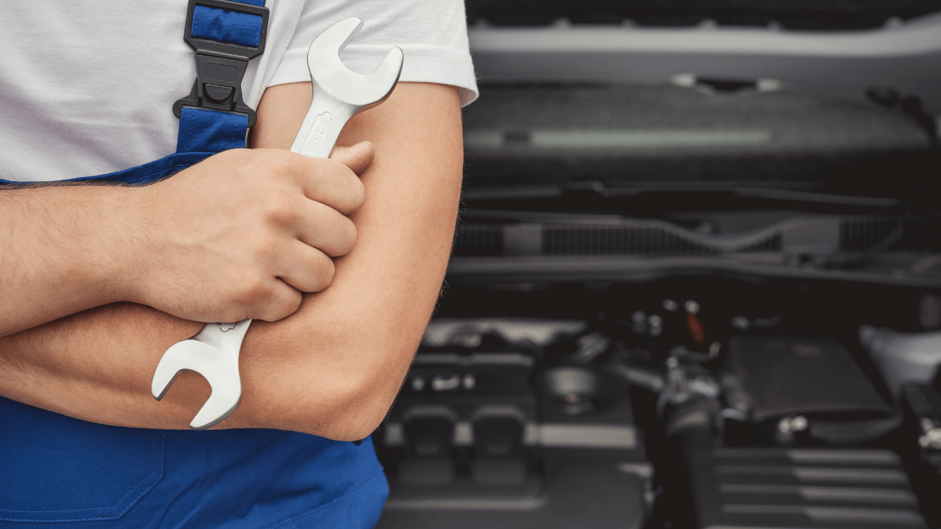 A mechanic holding a wrench in front of a car. 