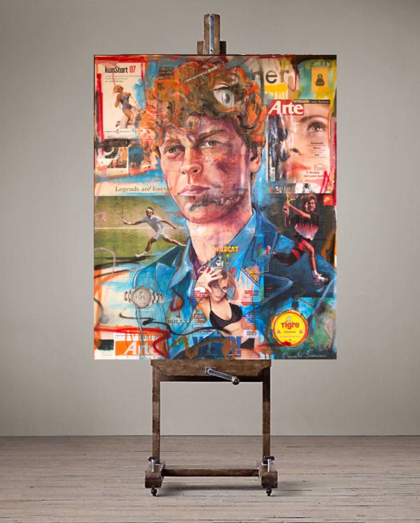 Un ritratto a collage con tecnica mista di una persona con i capelli ricci, posto su un cavalletto di legno su uno sfondo neutro da studio.