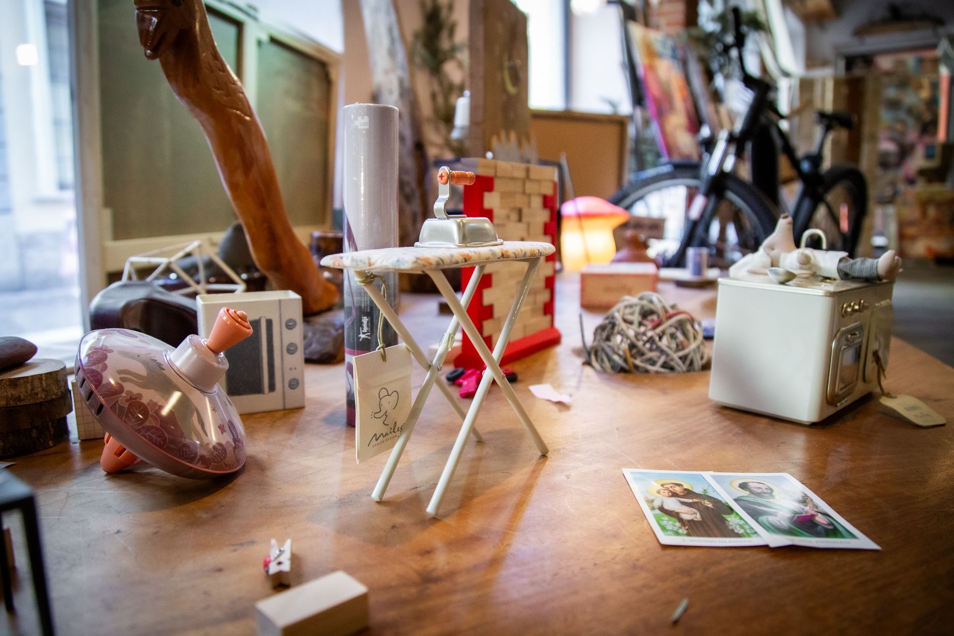 Un tavolo di legno ingombro di giocattoli in miniatura e oggetti decorativi, tra cui un minuscolo asse da stiro, una bicicletta e ninnoli.