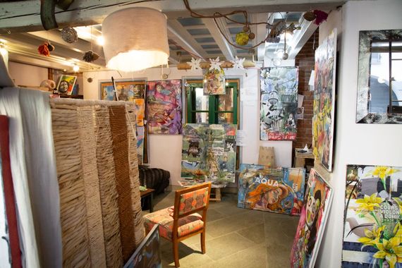 Uno studio d'arte pieno di dipinti colorati, una sedia di legno e pannelli con texture sotto lampade a sospensione.