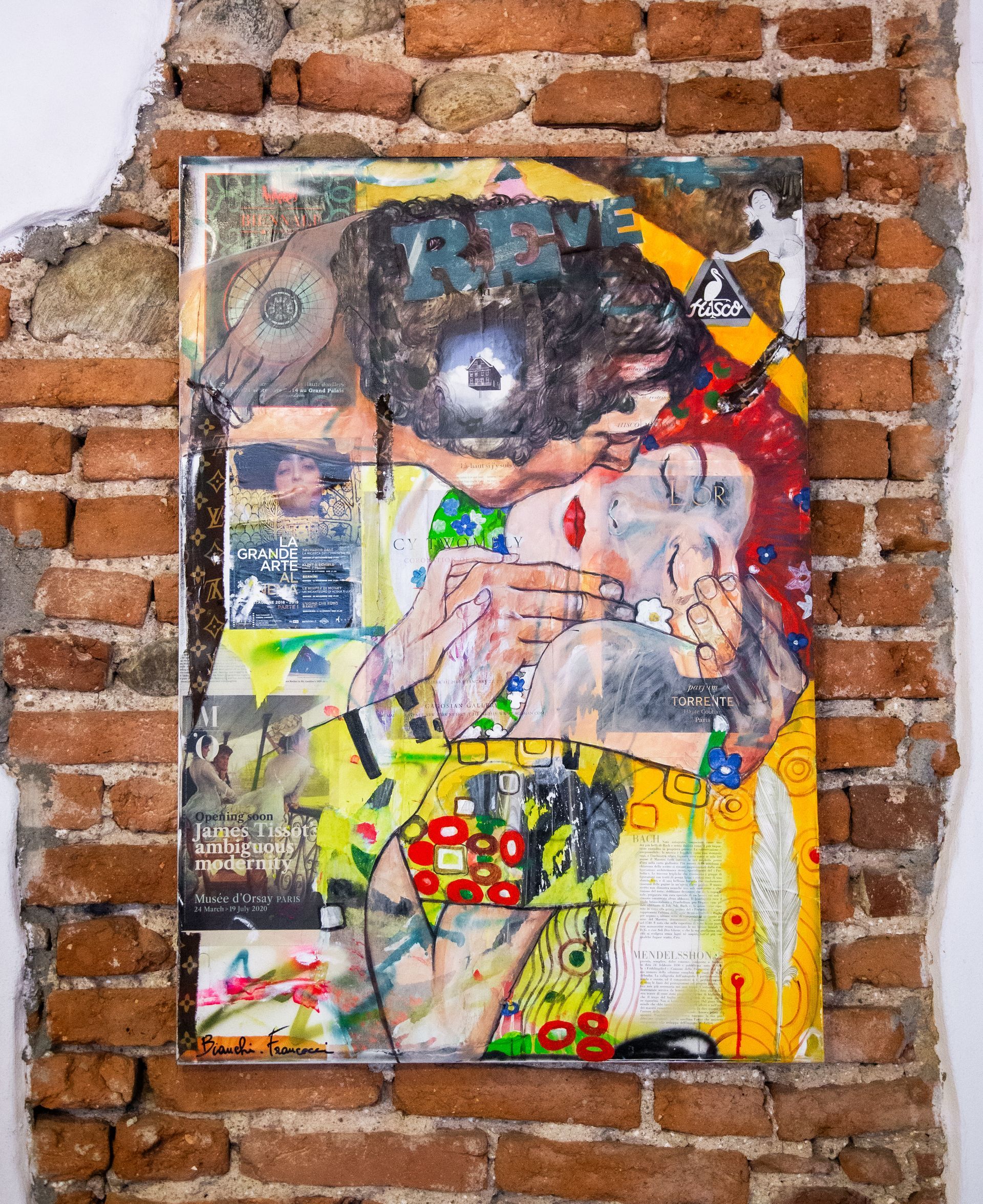 Un'opera d'arte vivace, realizzata con tecniche miste e composta da un occhio centrale, motivi astratti e testo, esposta su un muro di mattoni.