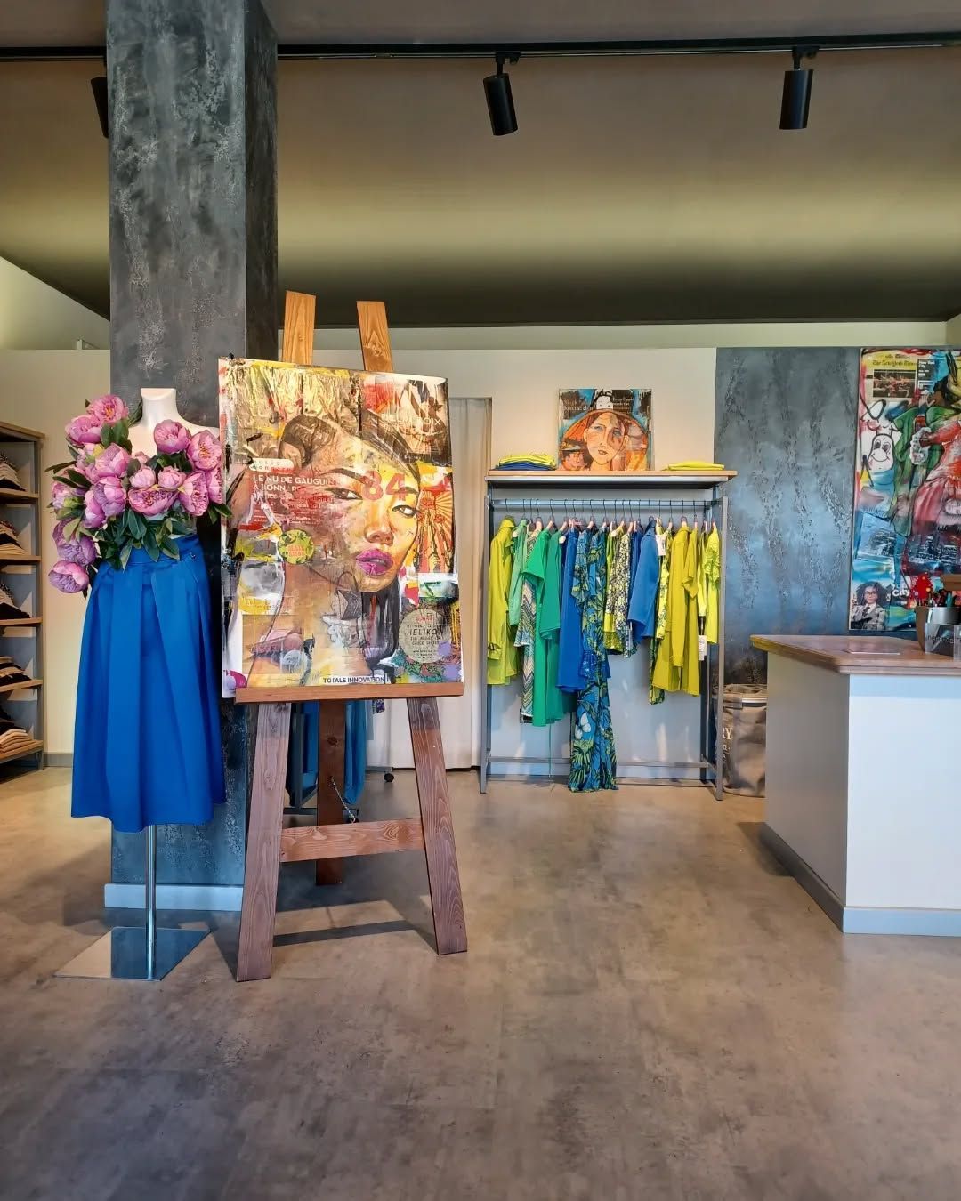 L'interno di una boutique presenta un ritratto su un cavalletto, una gonna blu su un manichino e abiti colorati su una gruccia.