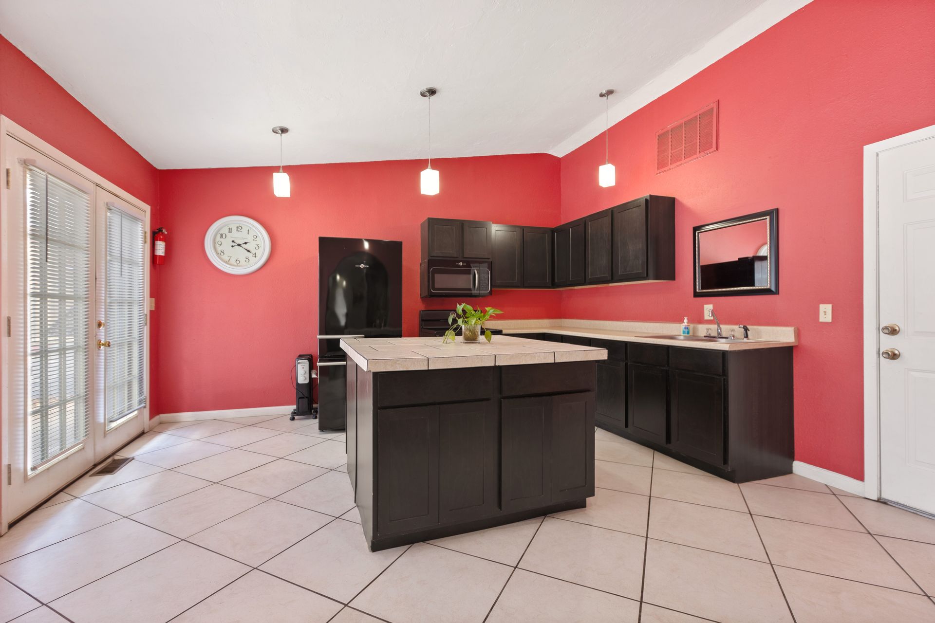 Red kitchen with dark cabinets, black oven, refrigerator, microwave, and island.