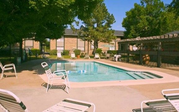 A swimming pool surrounded by lounge chairs, next to a building and trees.