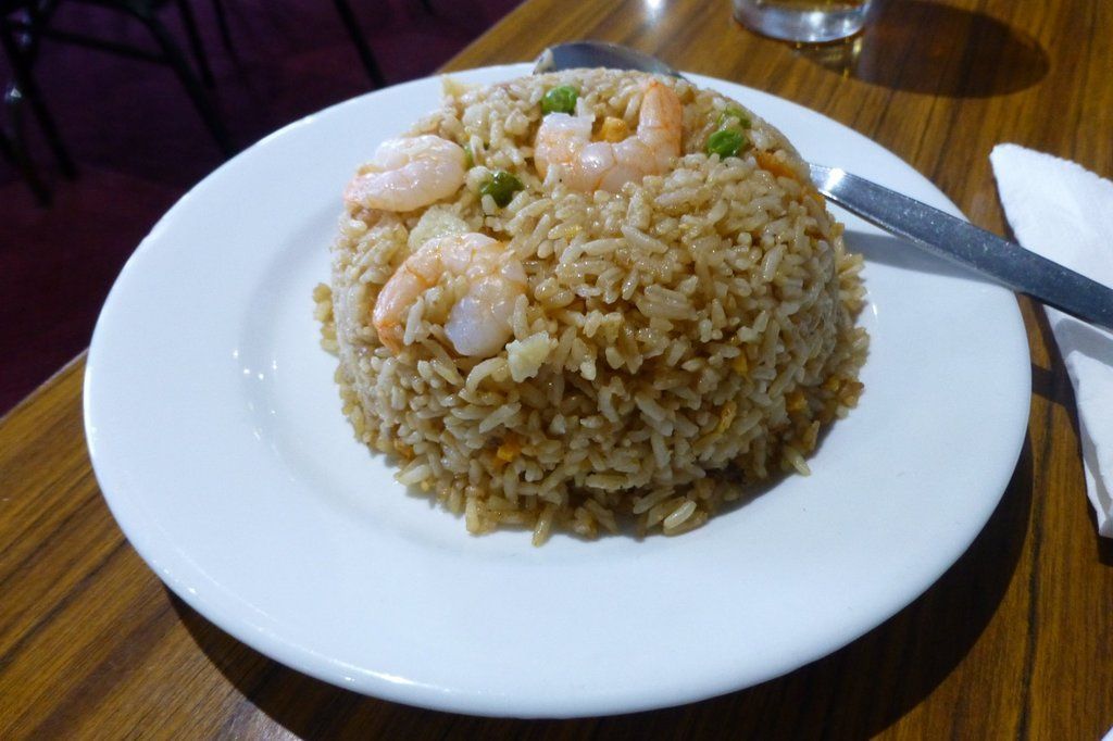 A plate of rice with prawns and peas on a wooden table