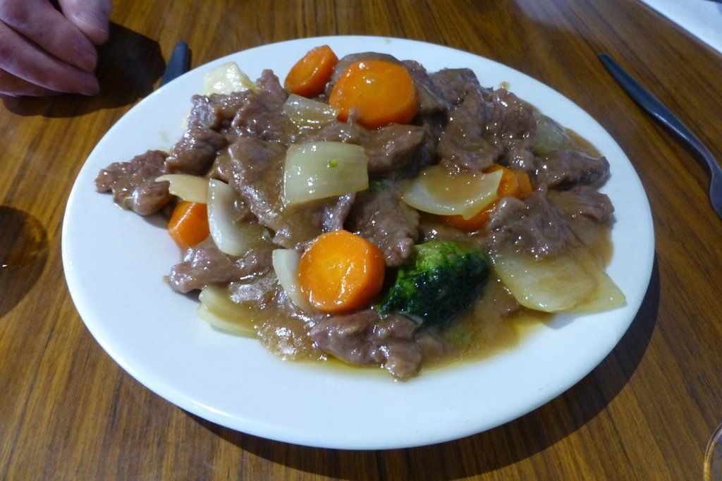A white plate topped with meat and vegetables on a wooden table
