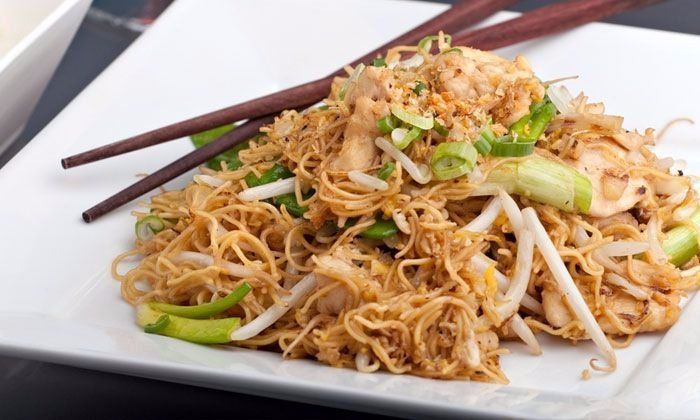 A white plate topped with noodles and chopsticks on a table.