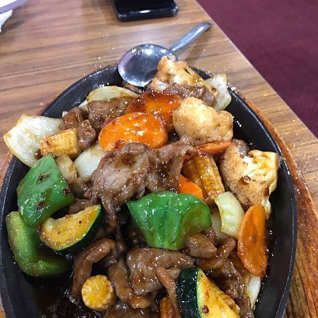 A plate of food with meat, vegetables and a spoon on a wooden table.