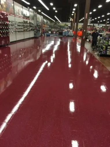 Red, shiny floor in a store, reflecting overhead lights. People browse shelves in the background.