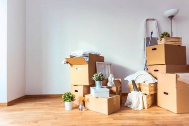 Cardboard boxes and miscellaneous items stacked on wooden floor, ready for moving.