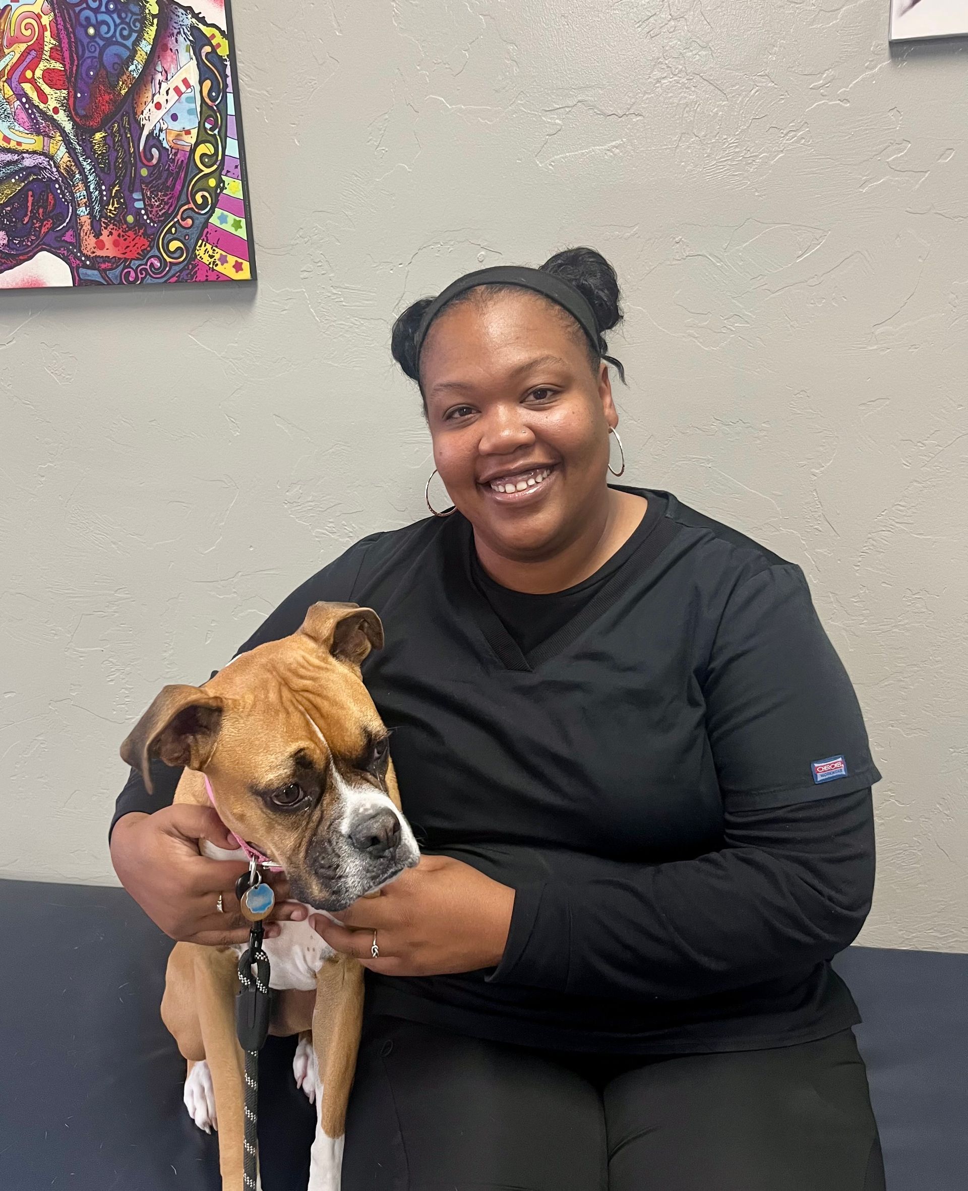 Woman in black scrubs hugs a tan and white dog. They sit on a blue bench in front of a gray wall. Woman in black scrubs hugs a tan and white dog. They sit on a blue bench in front of a gray wall.