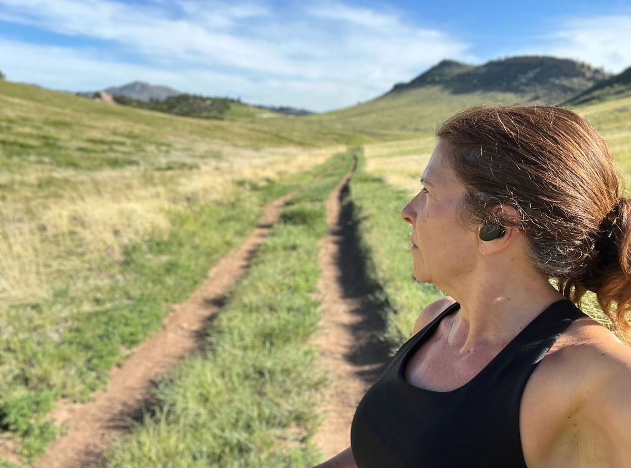 A woman wearing headphones is standing on a dirt road in a field.