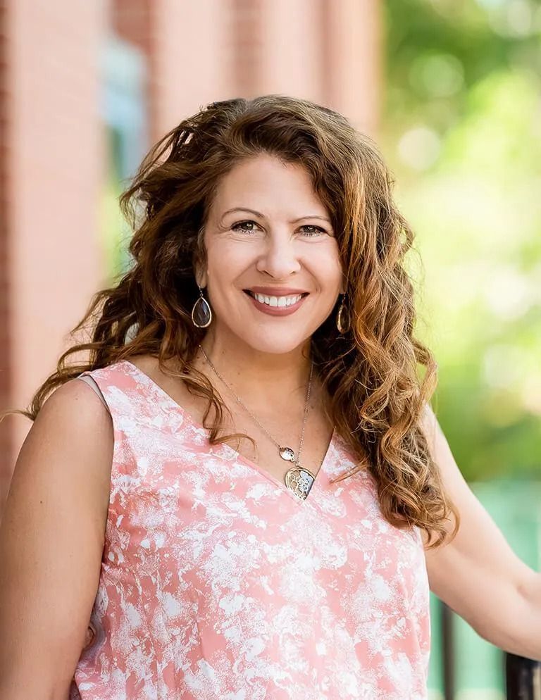 A woman in a pink top and necklace is smiling for the camera.