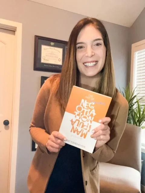 A woman in a brown jacket is holding a book in her hands