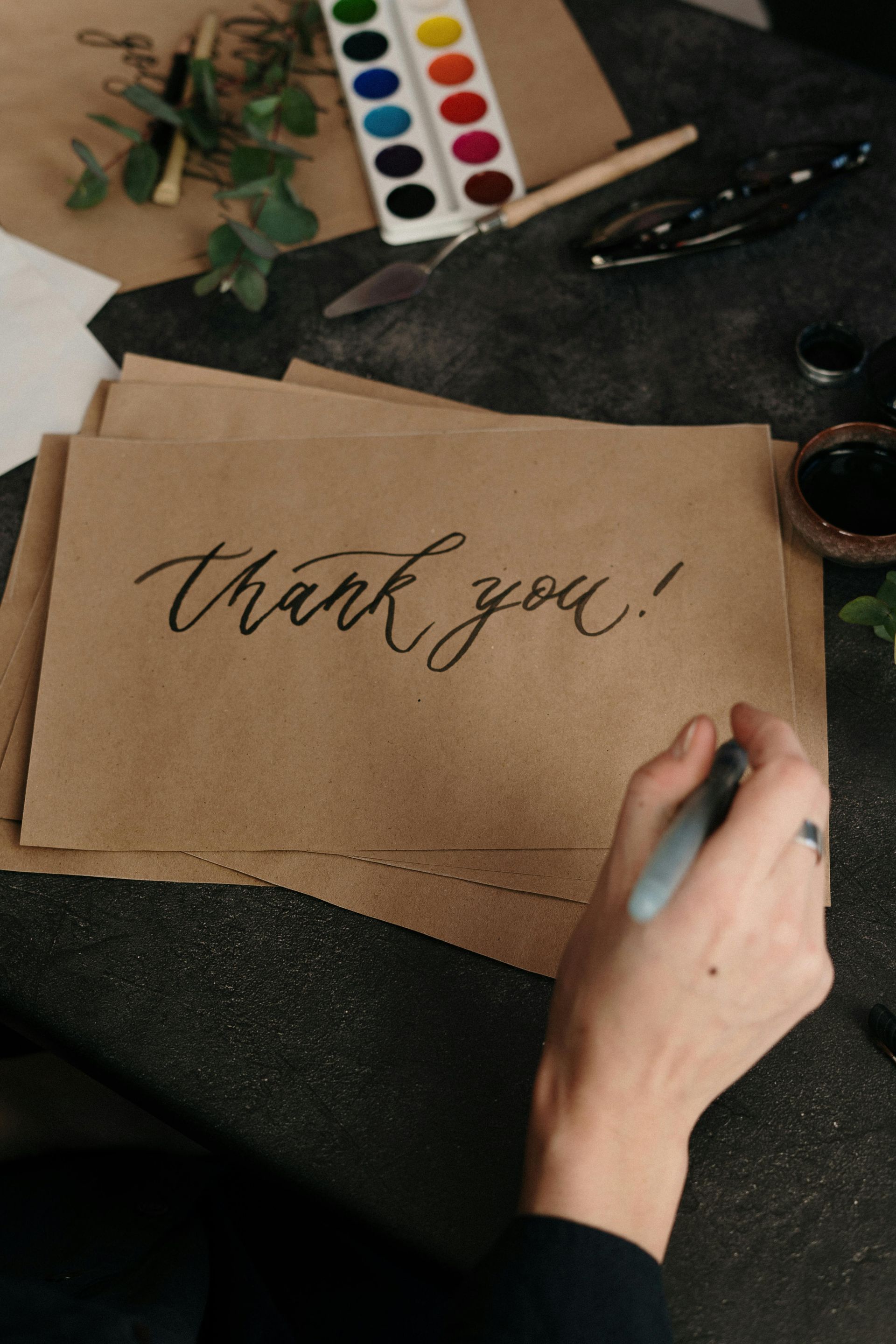 A person is writing a thank you card on a piece of brown paper.