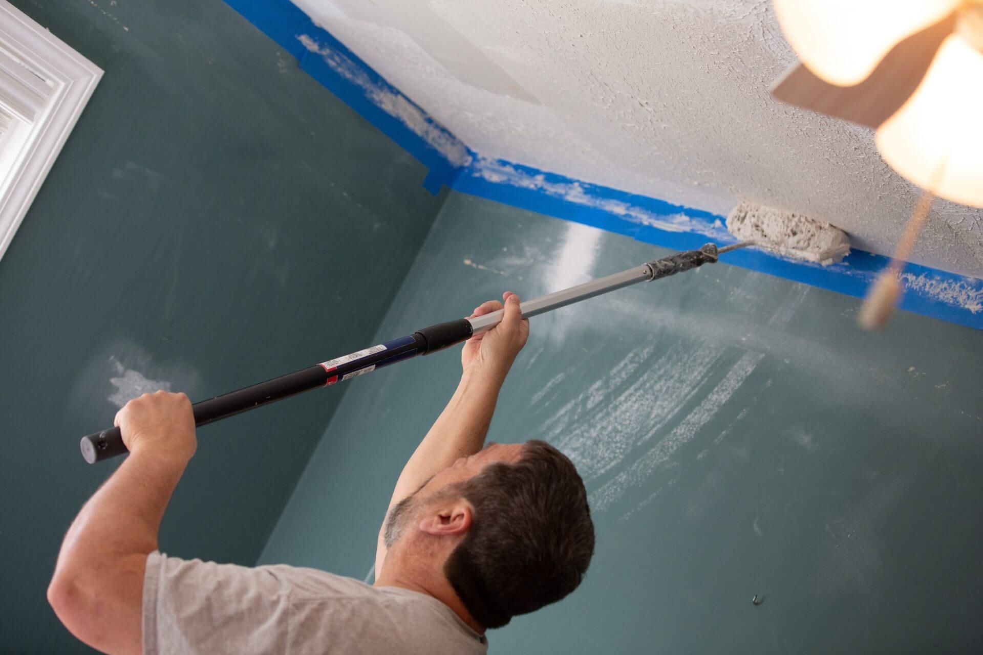 Painting the ceiling of a room with a paint roller.