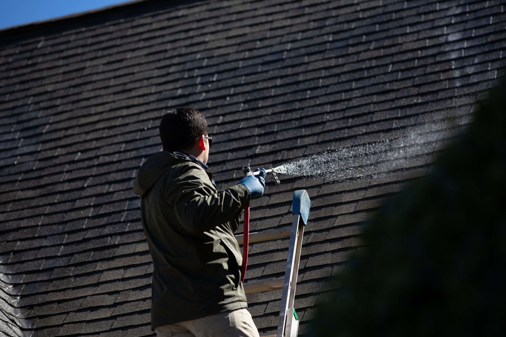 A man is cleaning the roof of a house with a hose.