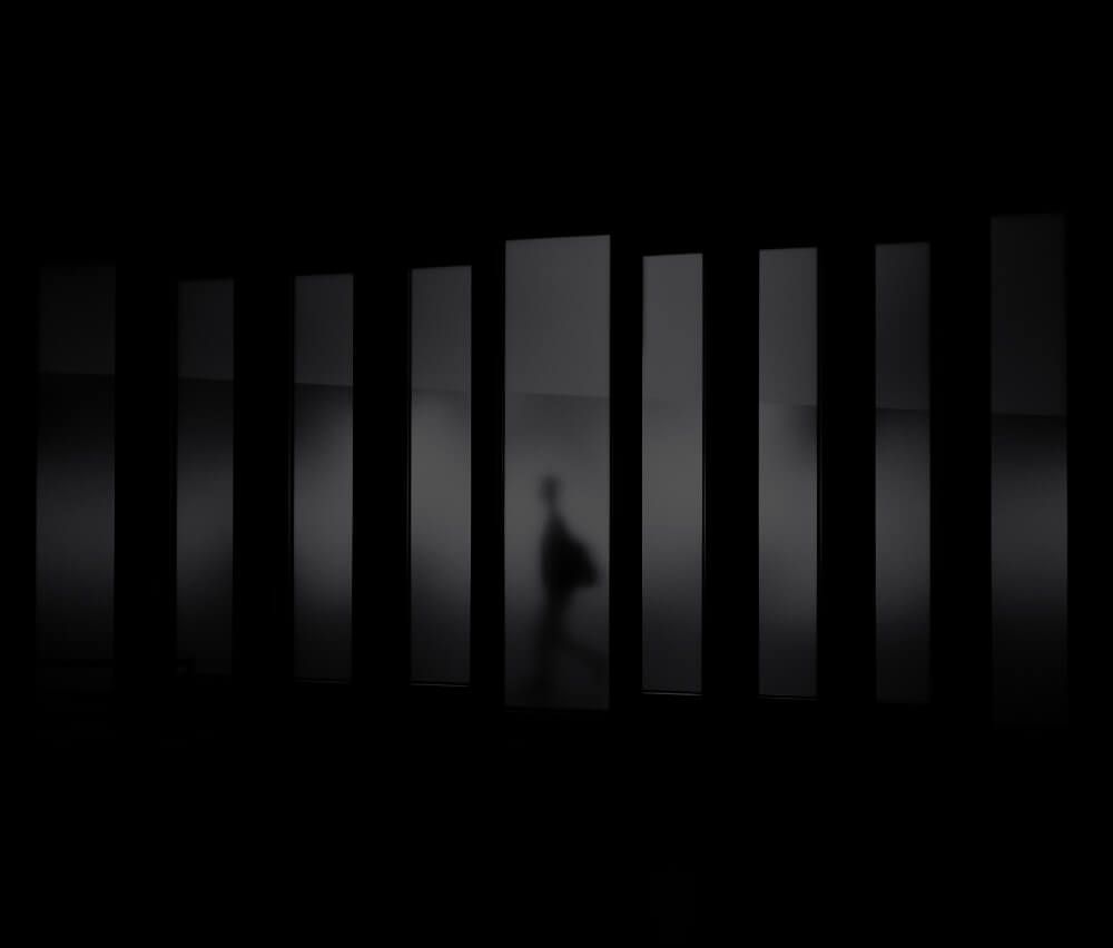 A shadow of a person is behind bars in a dark room.