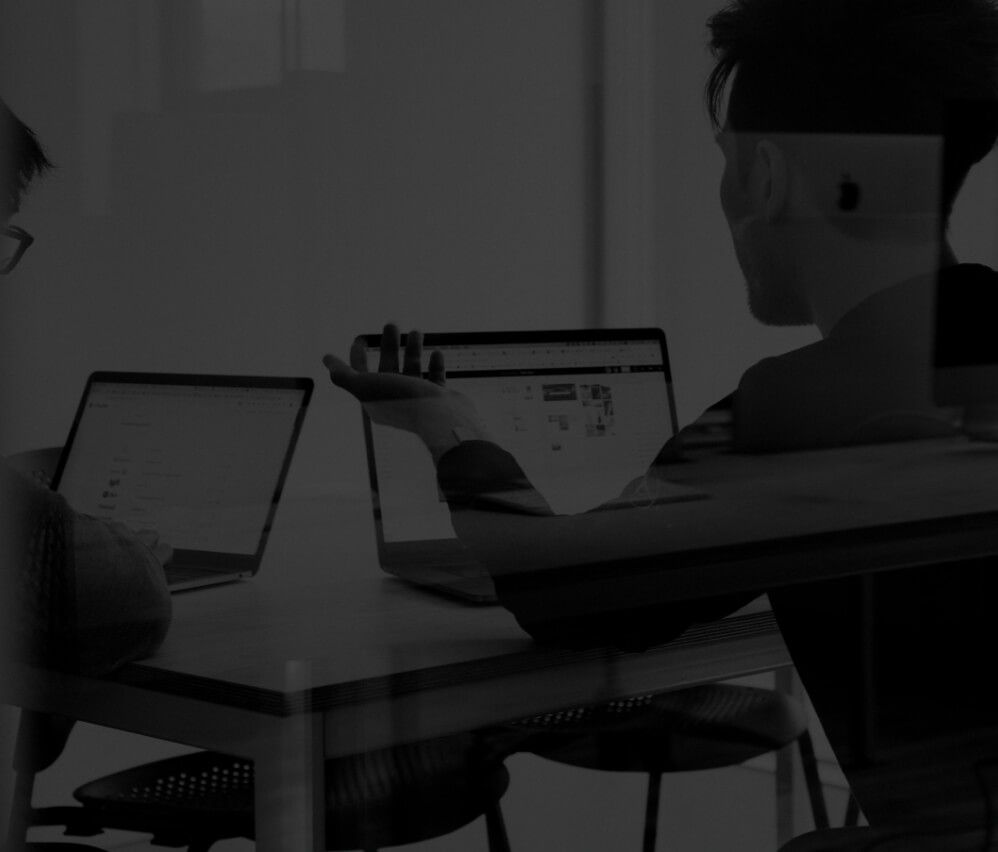 Two men are sitting at a table with laptops.