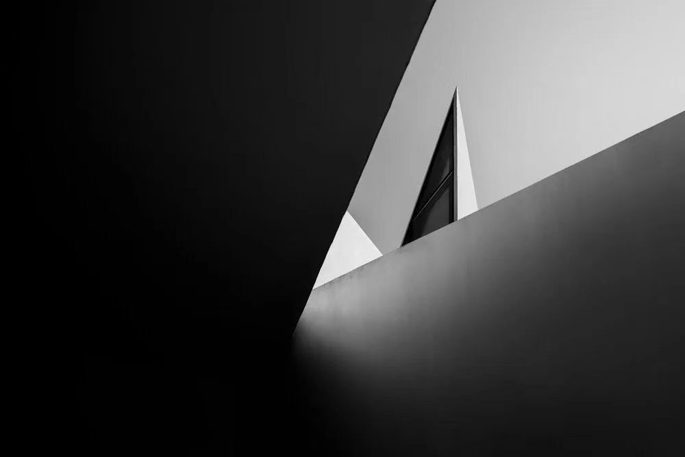 Black and white abstract architectural photo with sharp angles. A triangular window is visible.
