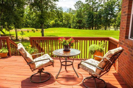 Patio with two cushioned chairs, round table, and flower centerpiece overlooking a green lawn and trees