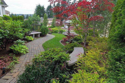 Lush landscaped garden with curved stone paths, benches, and colorful red and green foliage