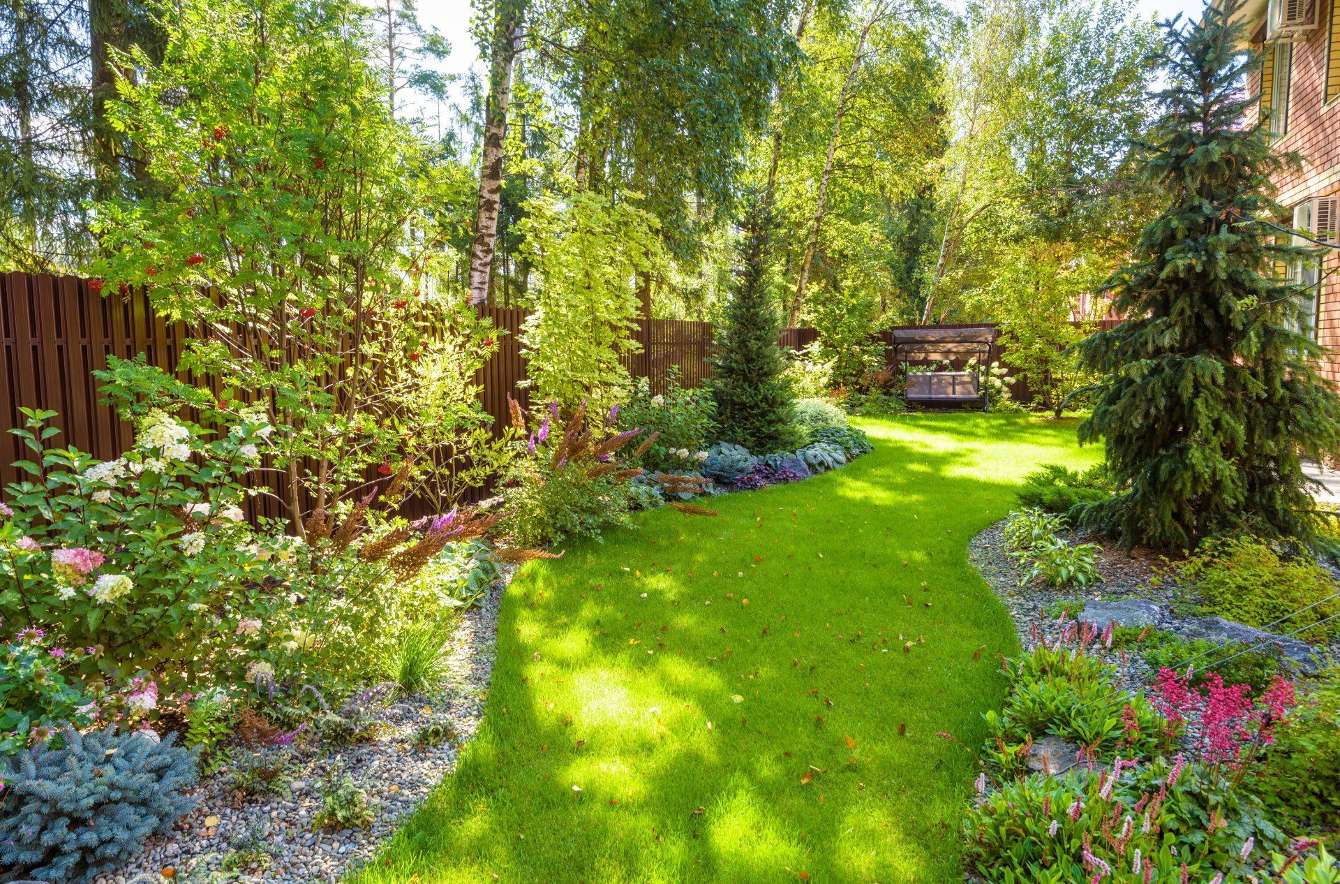 Sunlit garden path bordered by colorful flowers and lush green trees