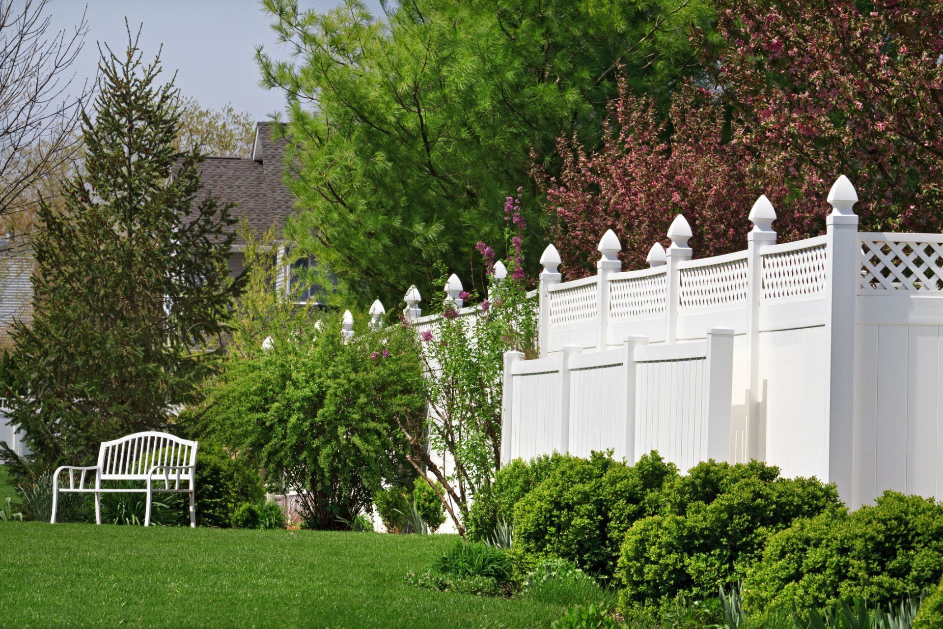 White fence and green lawn with a white bench in a landscaped garden.