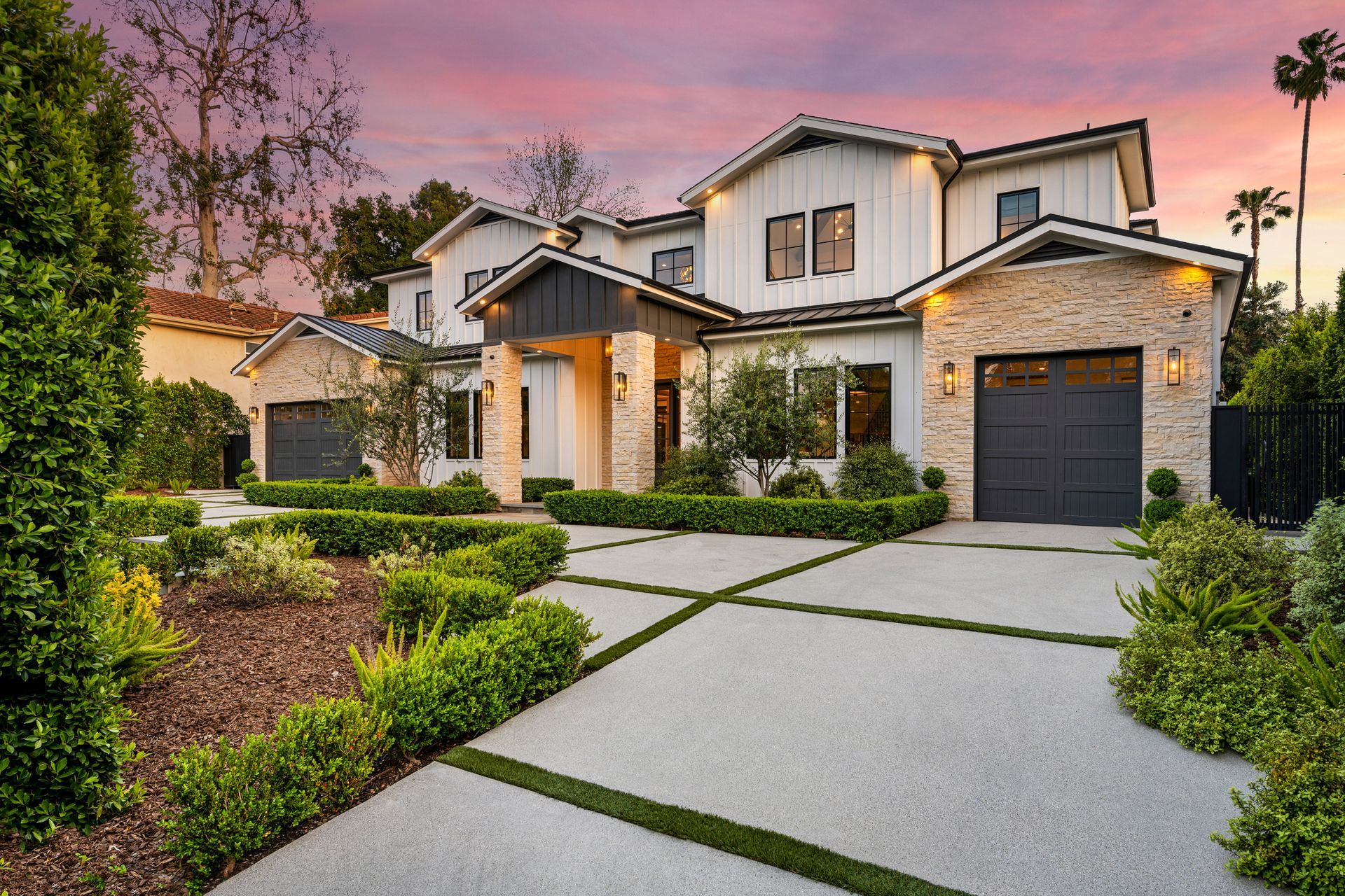 Modern two-story suburban house with stone exterior, front yard, and a driveway at sunset
