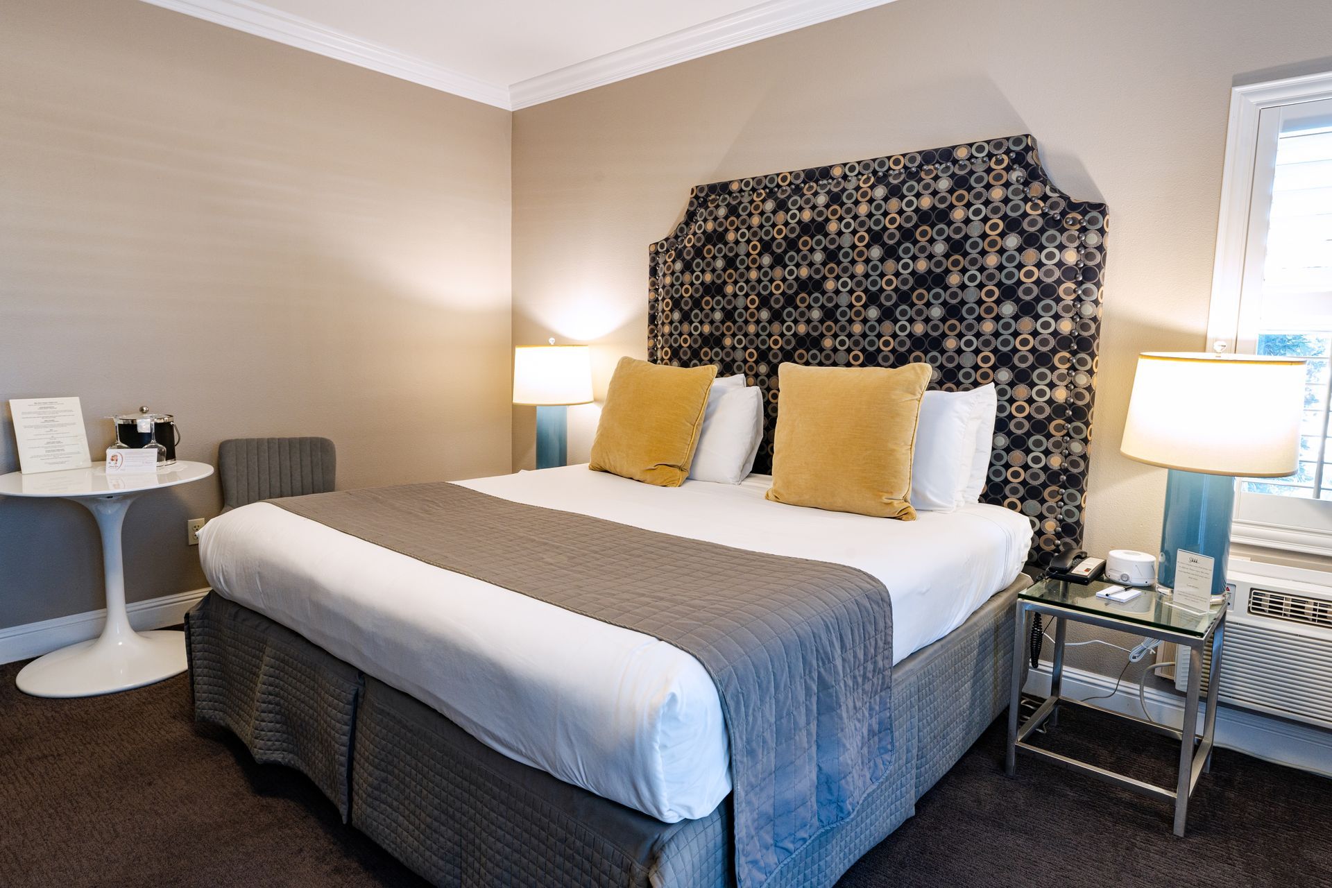 Hotel bedroom with a bed, lamps, side table, and white table with a chair.
