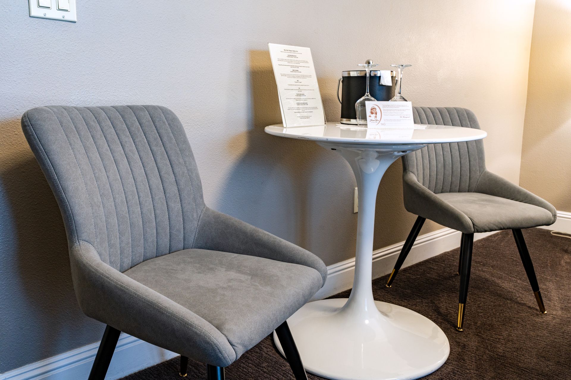 Two gray upholstered chairs and small round table with coffee setup in a room.