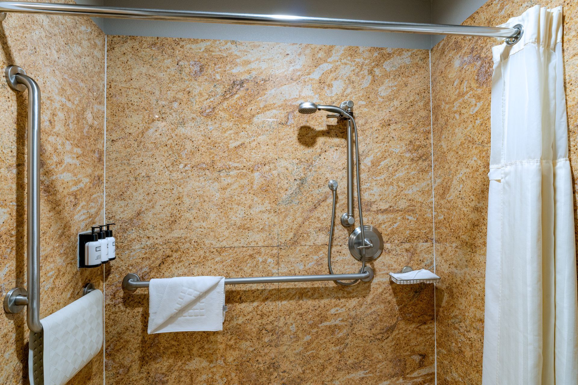 Accessible shower with grab bars and curtain. Warm-toned walls.