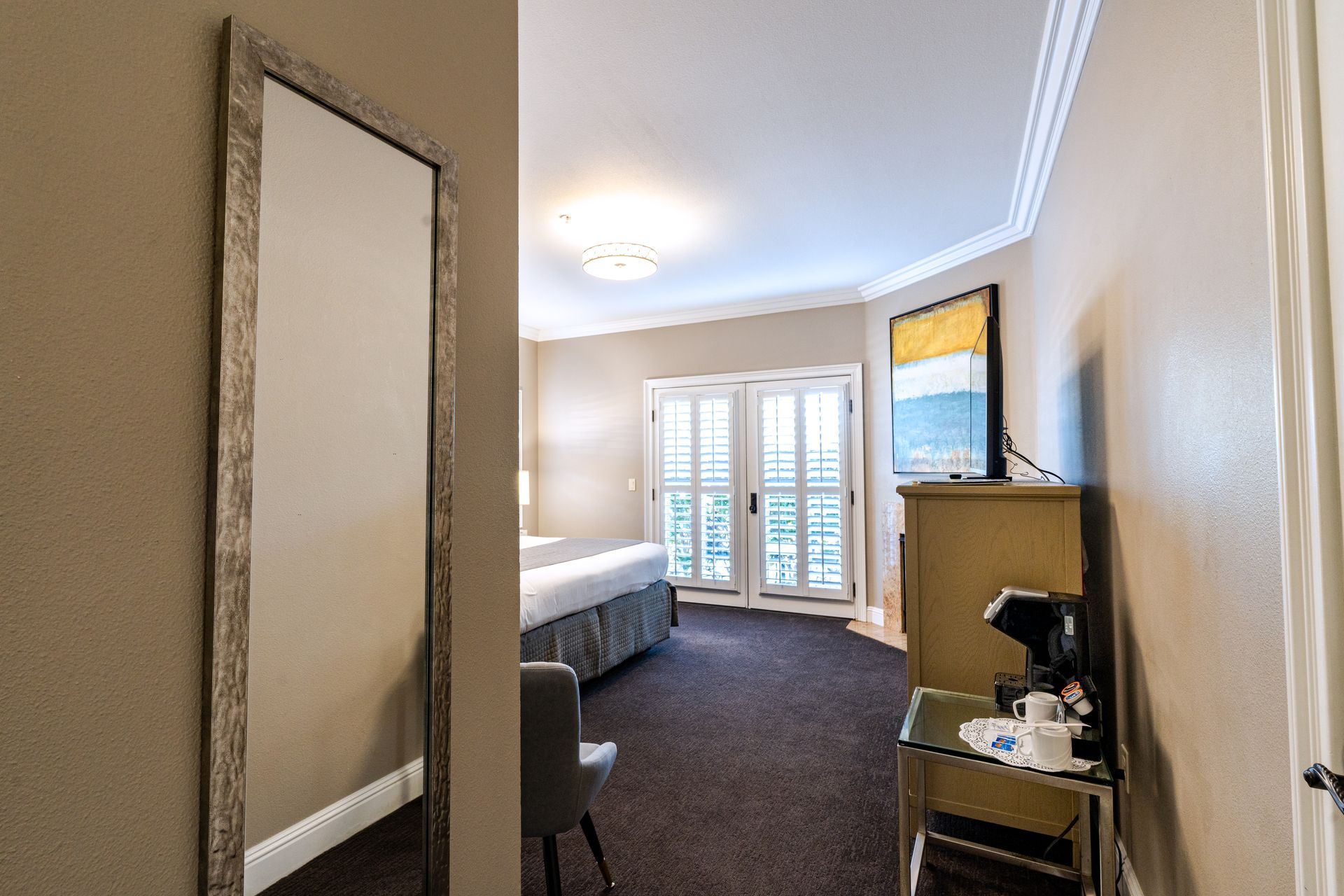 Hotel room interior with a full-length mirror, bed, closet, and balcony doors.