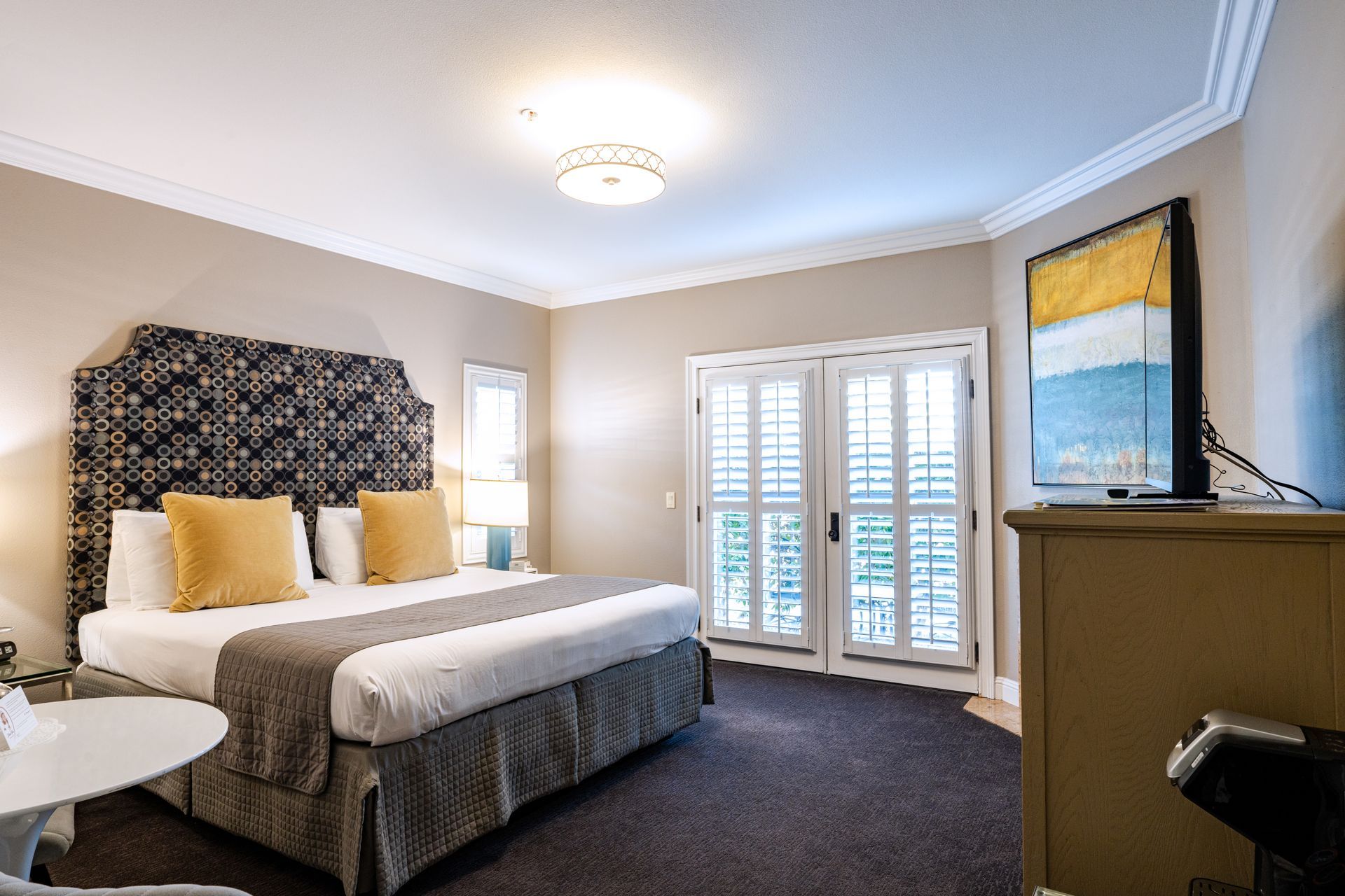 Bedroom with king-sized bed, patterned headboard, and shuttered doors. Neutral colors and artwork.