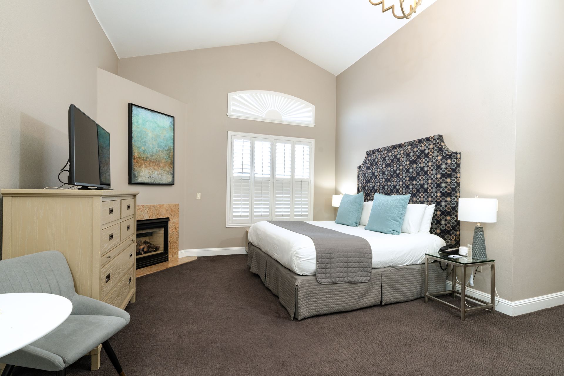 Hotel bedroom with a bed, TV, fireplace, and window with shutters.