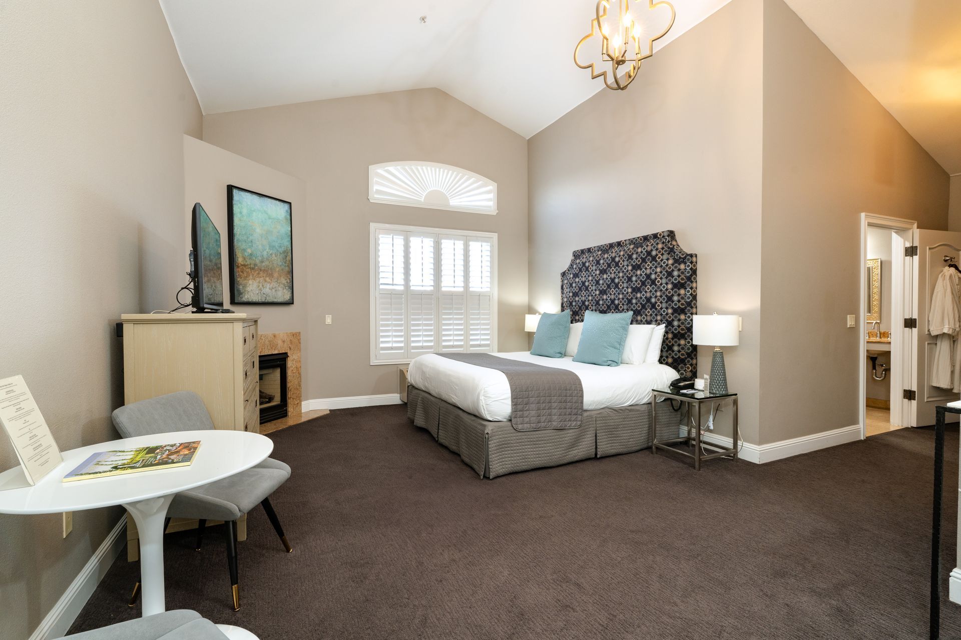 Hotel room with a bed, table, TV, and open bathroom.